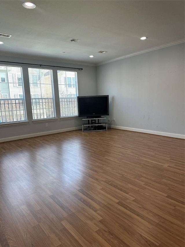 unfurnished living room with crown molding, wood finished floors, visible vents, and baseboards