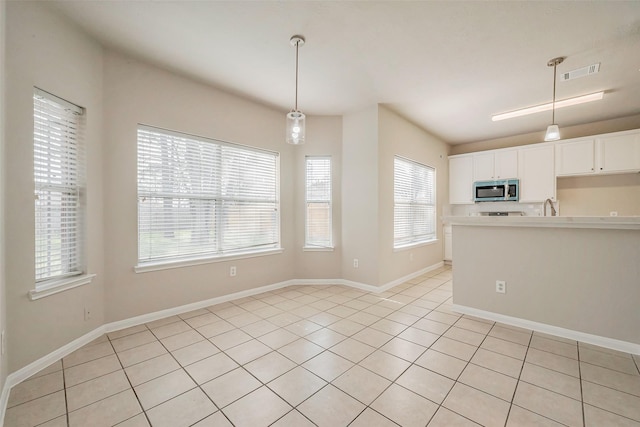 kitchen featuring stainless steel microwave, visible vents, light countertops, and hanging light fixtures