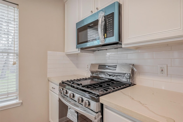 kitchen with light stone counters, stainless steel appliances, tasteful backsplash, and white cabinets