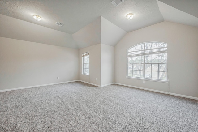 carpeted spare room featuring visible vents, a textured ceiling, baseboards, and lofted ceiling