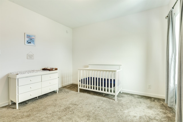 bedroom with baseboards, a nursery area, and carpet flooring