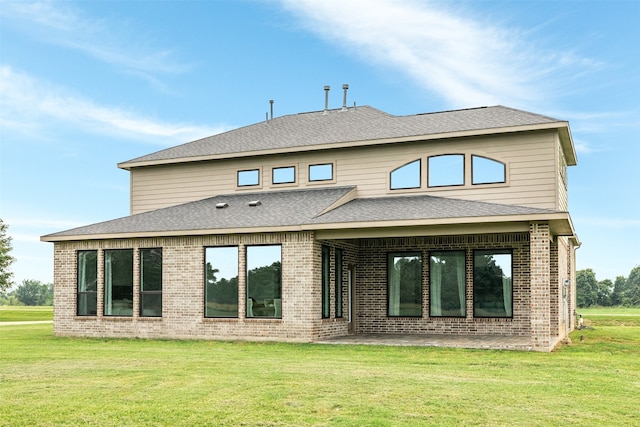 back of property featuring a lawn, a shingled roof, brick siding, and a patio area