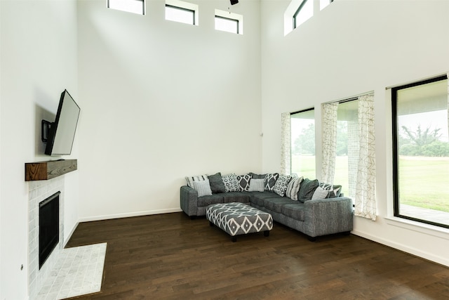 living area with a tiled fireplace, dark wood finished floors, baseboards, and a towering ceiling