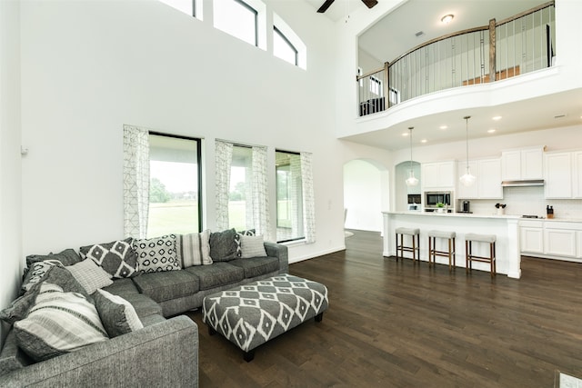 living room with a ceiling fan, plenty of natural light, dark wood-style floors, and arched walkways