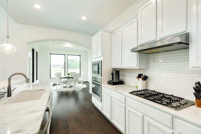 kitchen with arched walkways, stainless steel appliances, a sink, under cabinet range hood, and white cabinetry