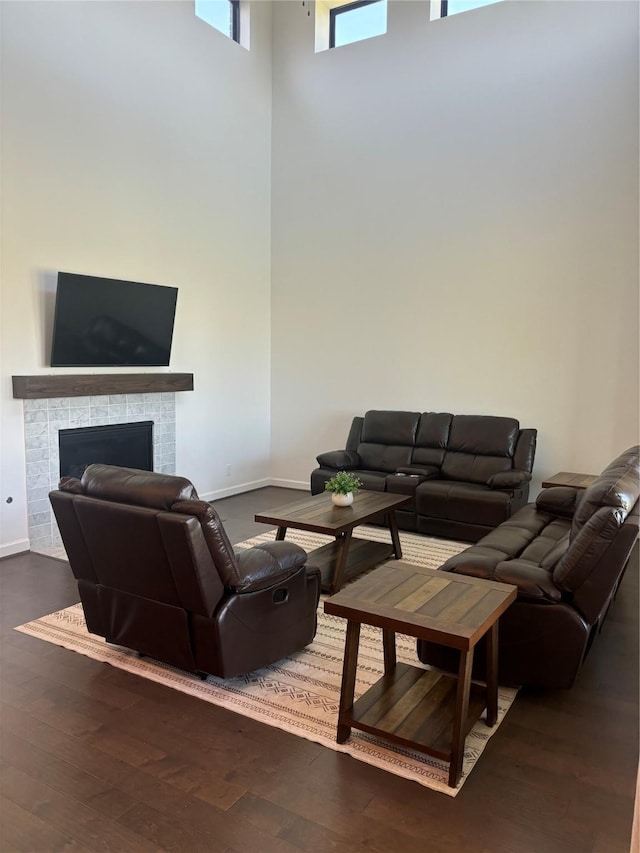 living area with a tiled fireplace, dark wood-type flooring, a high ceiling, and baseboards