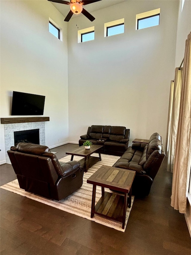 living room with baseboards, a ceiling fan, a high ceiling, and a tiled fireplace