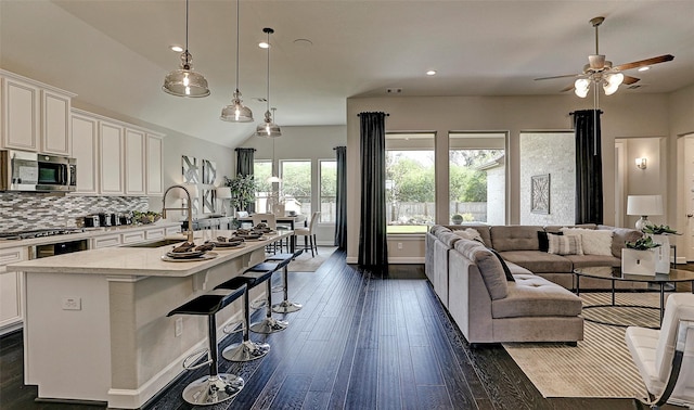 kitchen featuring a sink, stainless steel microwave, backsplash, dark wood-style floors, and open floor plan