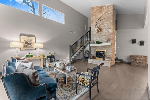 living room featuring stairway, wood finished floors, baseboards, a high ceiling, and a brick fireplace