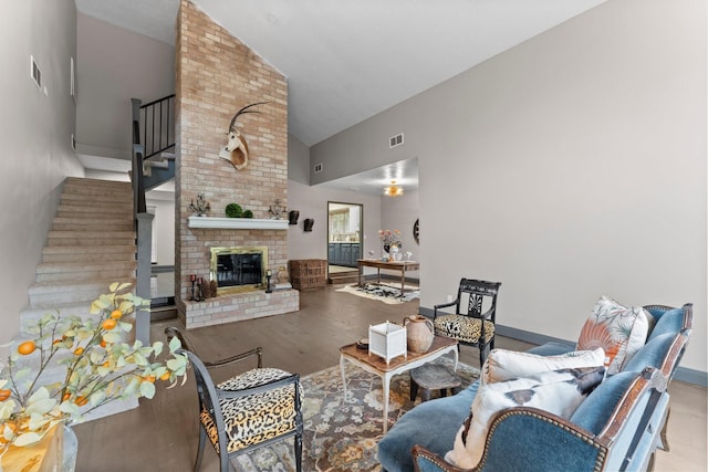 living room featuring visible vents, high vaulted ceiling, wood finished floors, stairway, and a brick fireplace