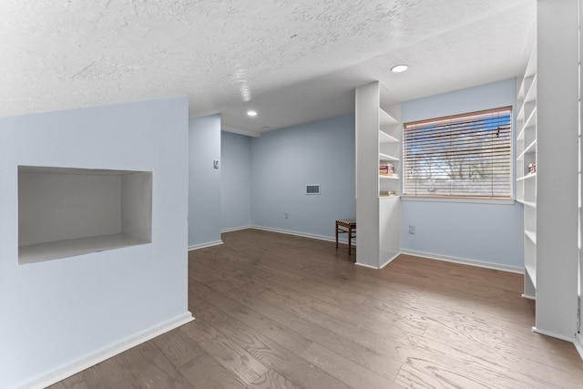 interior space with visible vents, baseboards, a textured ceiling, and wood finished floors