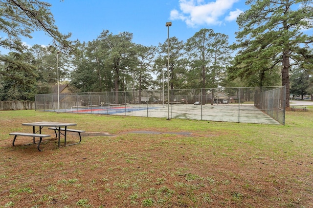 view of property's community with a tennis court, fence, and a lawn