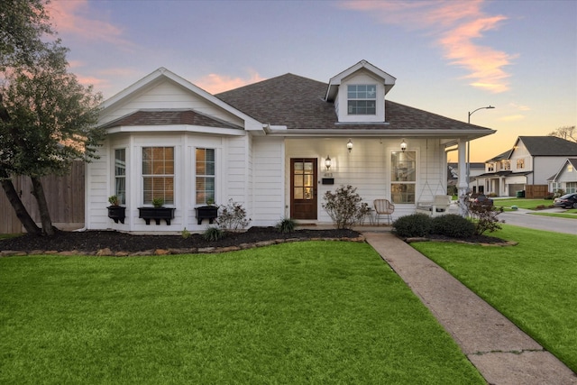 view of front of house with a porch, a shingled roof, and a front lawn