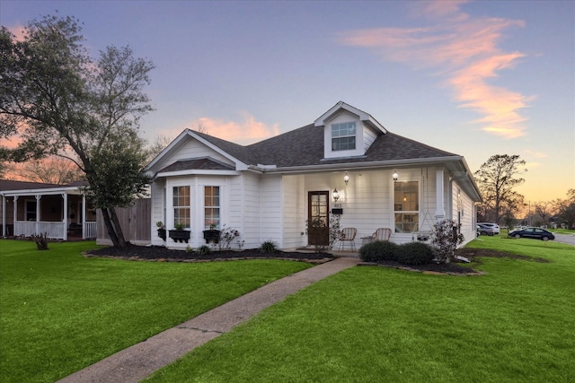 view of front of property with a front yard, covered porch, and a shingled roof