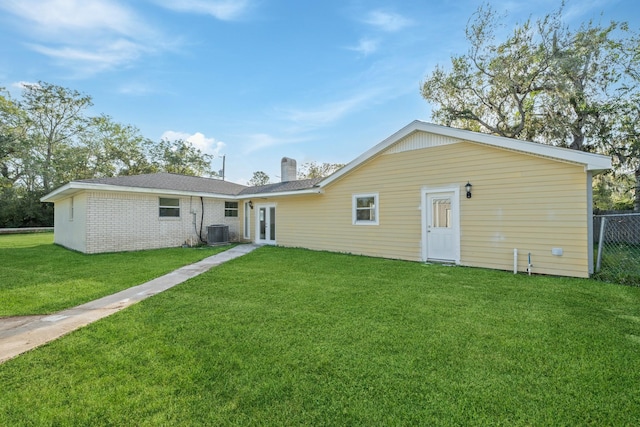 rear view of property featuring central AC unit, a chimney, french doors, a lawn, and brick siding