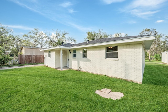 rear view of house with a yard, fence, and brick siding