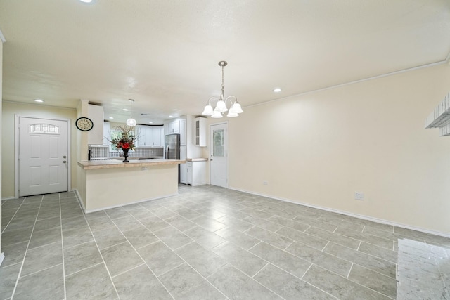 kitchen featuring open floor plan, a peninsula, freestanding refrigerator, a notable chandelier, and white cabinets