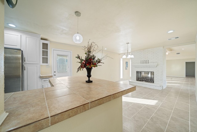 kitchen featuring visible vents, tile countertops, a fireplace, freestanding refrigerator, and white cabinets