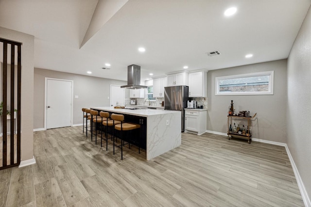 kitchen with island exhaust hood, light wood finished floors, backsplash, and freestanding refrigerator