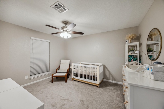 bedroom with visible vents, a textured ceiling, a crib, and carpet