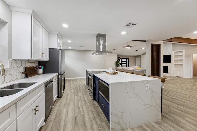 kitchen with visible vents, island exhaust hood, white cabinets, stainless steel appliances, and a sink