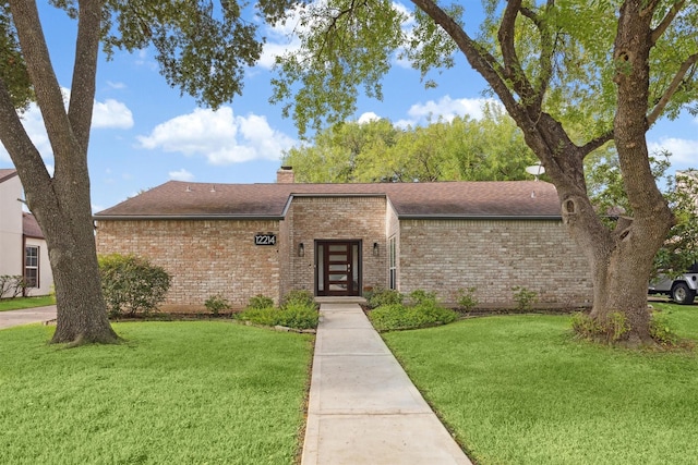 view of front of house featuring a shingled roof, a front yard, brick siding, and a chimney