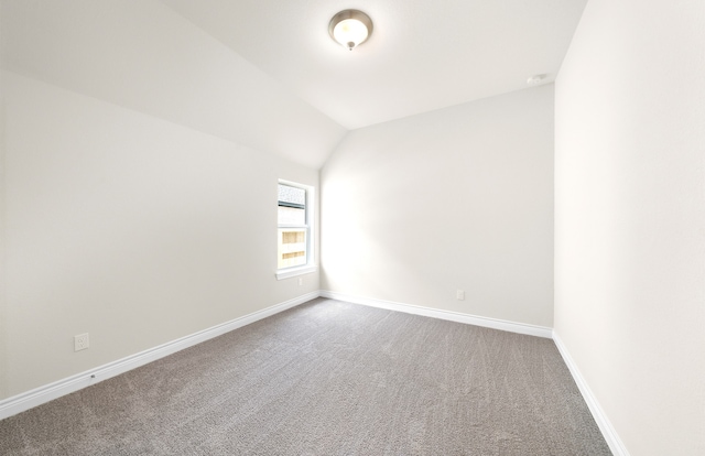 unfurnished room featuring vaulted ceiling, carpet, and baseboards