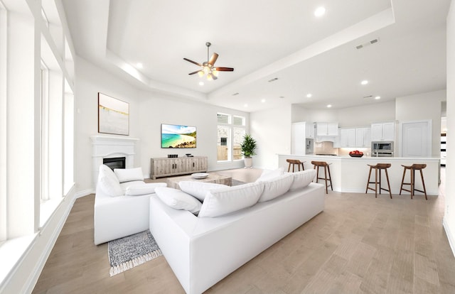 living room with a glass covered fireplace, a raised ceiling, recessed lighting, and visible vents