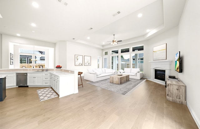 living room featuring recessed lighting, a raised ceiling, light wood-style floors, and a glass covered fireplace