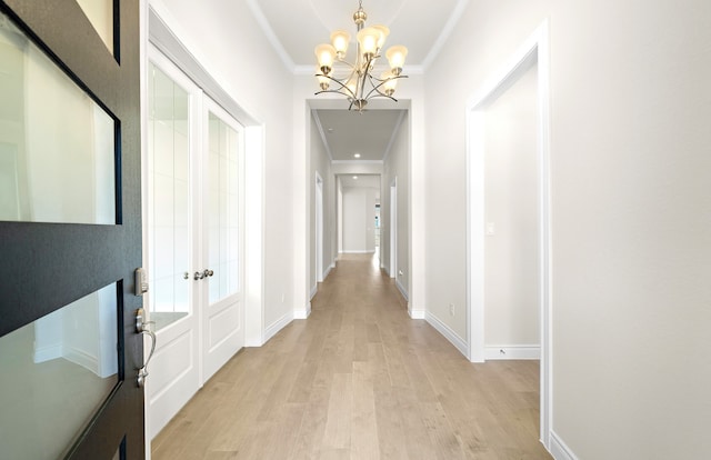 hall with baseboards, ornamental molding, light wood-style floors, french doors, and a chandelier