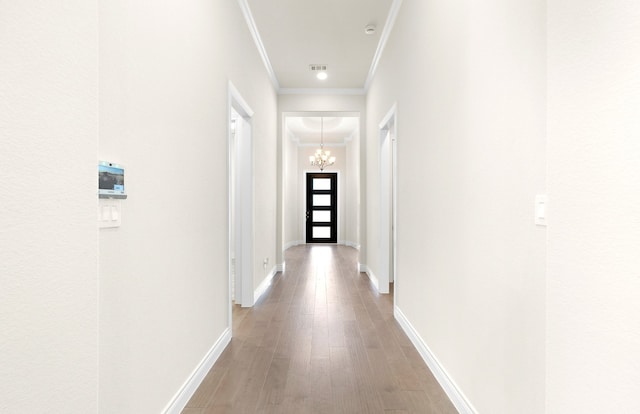 corridor featuring visible vents, light wood-style floors, crown molding, baseboards, and a chandelier