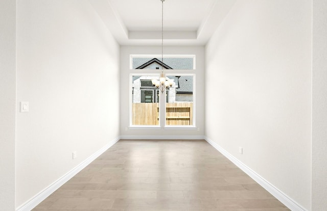 unfurnished dining area with light wood-style floors, a tray ceiling, plenty of natural light, and a notable chandelier