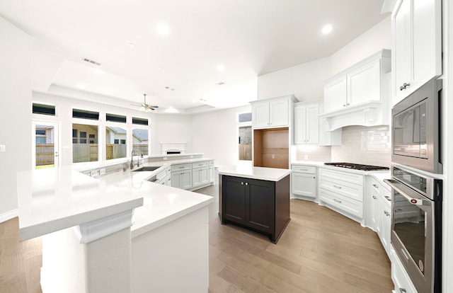 kitchen featuring a spacious island, light countertops, decorative backsplash, appliances with stainless steel finishes, and a sink