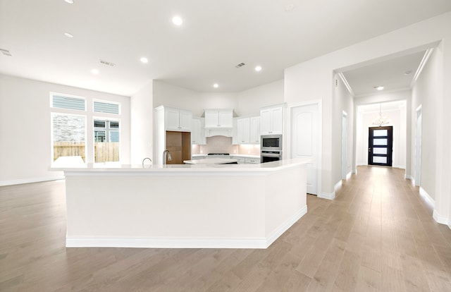 kitchen with stainless steel appliances, decorative backsplash, light countertops, white cabinets, and light wood-type flooring