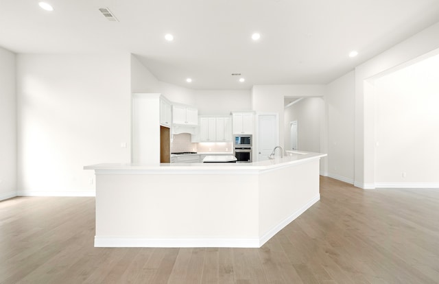 kitchen featuring stainless steel oven, built in microwave, white cabinets, and light wood finished floors