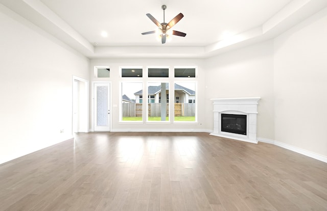 unfurnished living room featuring ceiling fan, light wood-style flooring, baseboards, and a glass covered fireplace