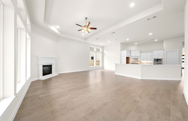 unfurnished living room featuring a tray ceiling, visible vents, a glass covered fireplace, and light wood finished floors