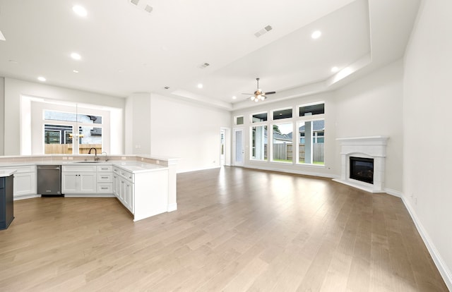 kitchen featuring light wood-type flooring, a sink, a tray ceiling, a glass covered fireplace, and open floor plan