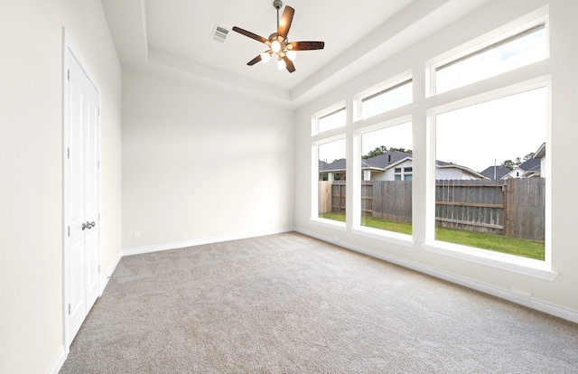 carpeted empty room with a tray ceiling, visible vents, baseboards, and ceiling fan