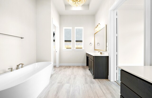 bathroom with a freestanding tub, a tray ceiling, an inviting chandelier, baseboards, and vanity