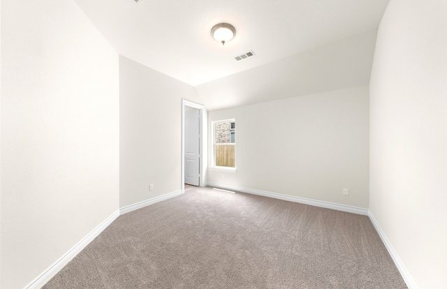 spare room featuring visible vents, carpet, baseboards, and vaulted ceiling