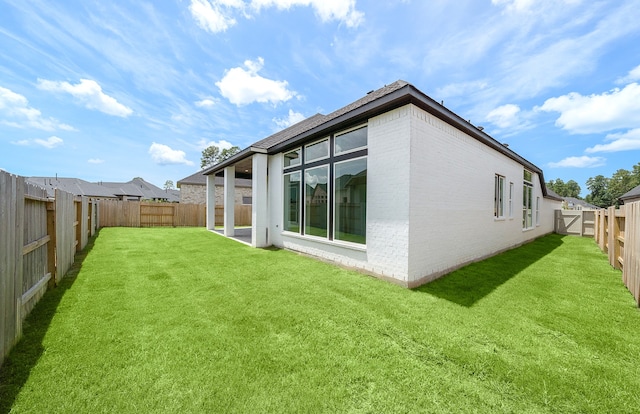 rear view of house with a yard, brick siding, and a fenced backyard