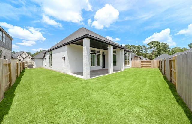 rear view of house with a patio area, a fenced backyard, a yard, and roof with shingles