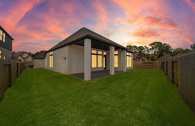 back of house at dusk with stucco siding, a patio, a lawn, and a fenced backyard