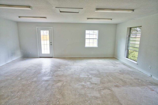 unfurnished room featuring a textured ceiling, attic access, and concrete floors