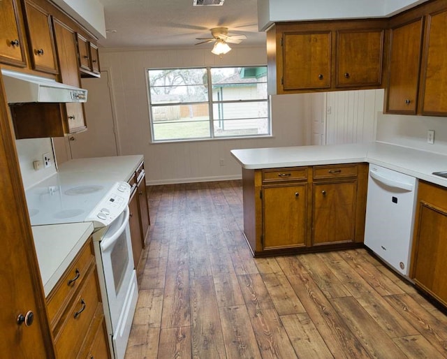 kitchen featuring under cabinet range hood, a peninsula, brown cabinetry, white appliances, and wood-type flooring