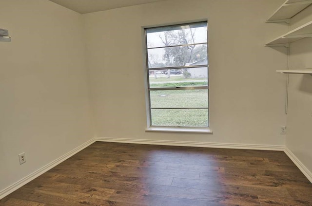 spare room featuring baseboards, dark wood-type flooring, and a healthy amount of sunlight