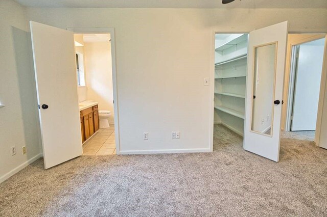 unfurnished bedroom with baseboards, ensuite bath, a spacious closet, a closet, and light carpet