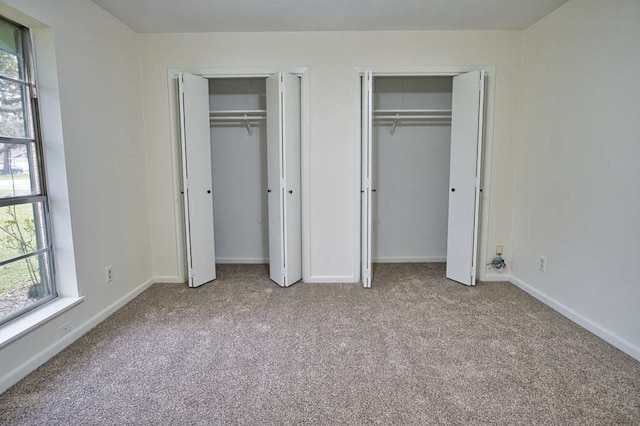 unfurnished bedroom with carpet flooring, multiple windows, two closets, and baseboards