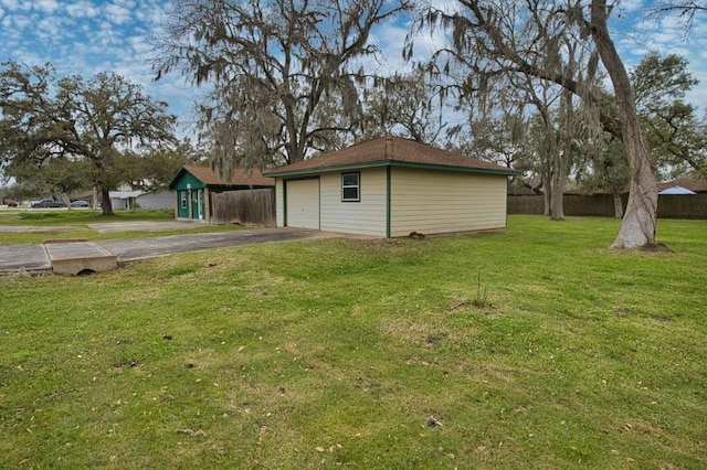 view of yard featuring aphalt driveway, a garage, an outbuilding, and fence